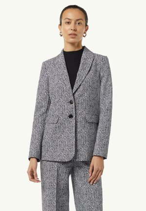 Blazer in tessuto pied-de-poule bianco e nero, con vestibilità strutturata, due bottoni, rever a scollo e tasche laterali. Abbinato a pantaloni coordinati.