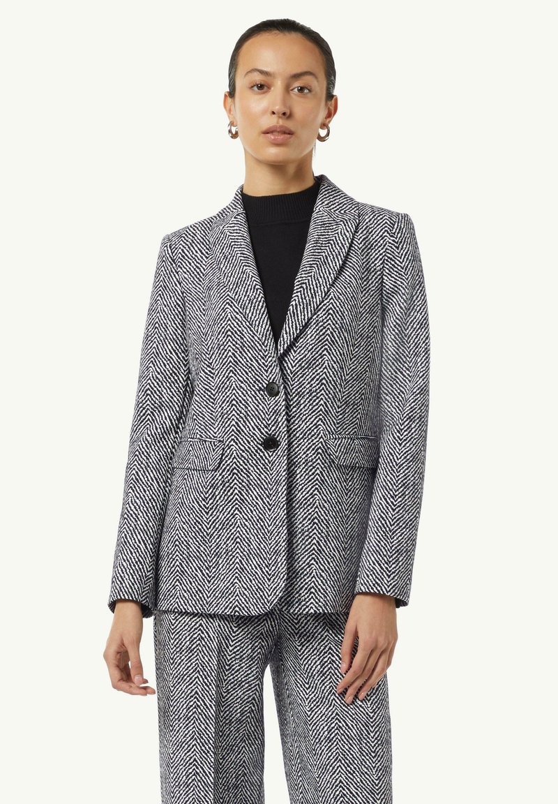 Karoblazer in Schwarz und Weiß, mit strukturierter Passform, zwei Knöpfen, Reverskragen und seitlichen Taschen. Kombiniert mit passenden Hosen.