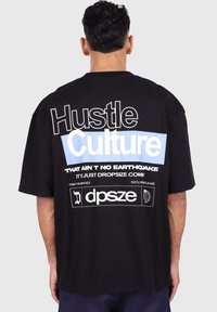 Crna oversized majica s hrabrim bijelim i svijetloplavim tekstom na leđima, na kojem piše "Hustle Culture" i grafički detalji.