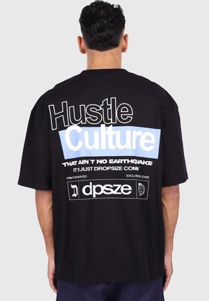 Black oversized t-shirt featuring bold white and light blue text on the back, displaying "Hustle Culture" and graphic details.