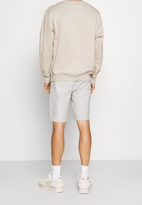 Beige sweatshirt, gråstribede shorts og lyse sneakers med hvide sokker. Fokus på komfort og afslappet design med simple former og bløde teksturer.