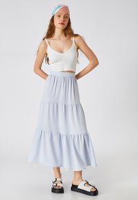Jupe maxi à volants bleu clair avec taille élastique, portée avec un crop top blanc à côtes et des sandales à plateforme noires avec des boucles.