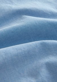 Tejido azul claro con una textura fina, que presenta patrones sutiles. El material parece suave, ligero y ligeramente arrugado.