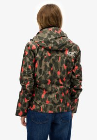Kurtka w kamuflażowym wzorze w zielonym i czerwonym kolorze. Posiada kaptur, zamek błyskawiczny, elastyczne mankiety oraz logo z tyłu. Wodoodporny materiał.