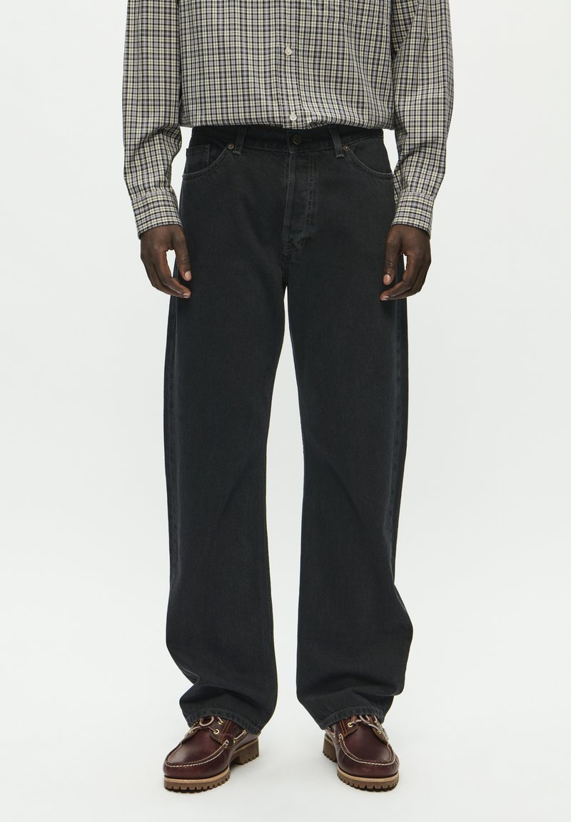 Laiad mustad teksad tekstuuri viimistlusega. Kombineeritud ruudulise nööbiga särgiga ja pruuni nahast kingadega, millel on dekoratiivsed paelad.