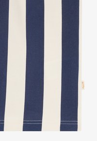 Τμήμα υφάσματος με κάθετες ρίγες σε ναυτικό μπλε και λευκό, και μια μικρή μπεζ ετικέτα στη δεξιά άκρη.