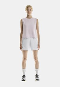 Lichtroze mouwloze top met een ronde hals, gecombineerd met witte shorts, gedragen met grijze sneakers en witte sokken met zwarte accenten.