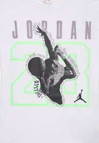 Valge T-särk, millel on must graafika korvpallurist, neoonroheline "23" ja tekst "JORDAN", ümber pildi on hallid motiveerivad fraasid.
