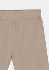 Calças bejes com um cós elástico, apresentando um tecido texturizado e bolsos laterais para maior funcionalidade.