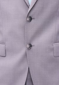 Κλειστό ανοιχτό γκρι σακάκι κοστουμιού με δύο σκούρα γκρι κουμπιά και τσέπες με καπάκι σε κάθε πλευρά.