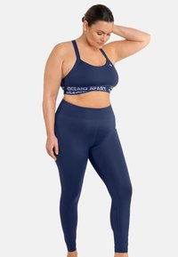 Reggiseno sportivo blu navy con fascia con logo e leggings a vita alta abbinati, entrambi realizzati in tessuto elastico, caratterizzati da una texture liscia e un design aderente.