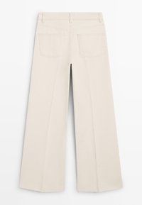 Pantalon en coton beige à jambes larges, avec une texture lisse, doté de deux poches arrière et d'une ceinture simple.