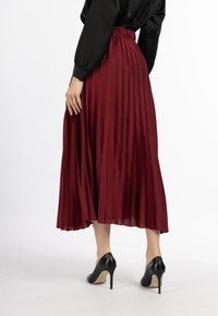 Fustă midi plisată roșie cu talie elastică, fabrică ușoară, asortată cu pantofi cu toc înalt negri, prezentată din spate.