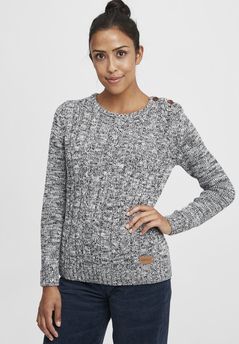 Pull en maille gris et blanc avec un col rond et des manches longues. Équipé de boutons bruns sur l'épaule et d'une patte en cuir avec un logo.