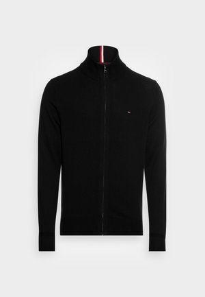 Pull noir zippé intégral avec col, poignets et ourlet côtelés, arborant un petit logo rouge, blanc et bleu sur la poitrine gauche.