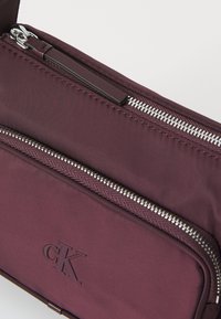 Borsa in nylon bordeaux con zip in tono argento, texture liscia, logo in rilievo e due scomparti con zip arricchiti da eleganti dettagli in pelle.