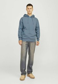 Blauwe hoodie met een voorzak, trekkoordcapuchon, ribgebreide manchetten, gecombineerd met lichtblauwe jeans en beige schoenen. Eenvoudig, casual ontwerp.