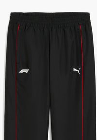 Schwarze Sporthosen mit elastischem Bund, ausgestattet mit roten seitlichen Streifen. Enthält ein kleines weißes Logo auf dem linken Oberschenkel und ein Logo auf der rechten Seite.