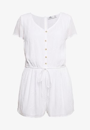 Combinaison en coton blanc avec des manches courtes, décolletée en V, fermeture à boutons, taille élastique et détails de broderie décorative sur le tissu.