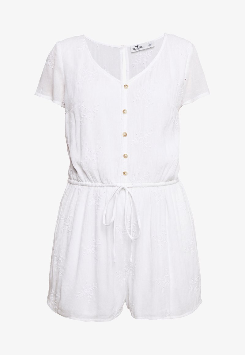 Biały bawełniany kombinezon z krótkimi rękawami, dekoltem w serek, zapięciem na guziki, elastyczną talią i ozdobnymi haftami na materiale.