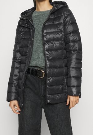 Person wearing a black puffer jacket over a gray sweater, black belt with gold buckle, and dark gray jeans against a plain background.