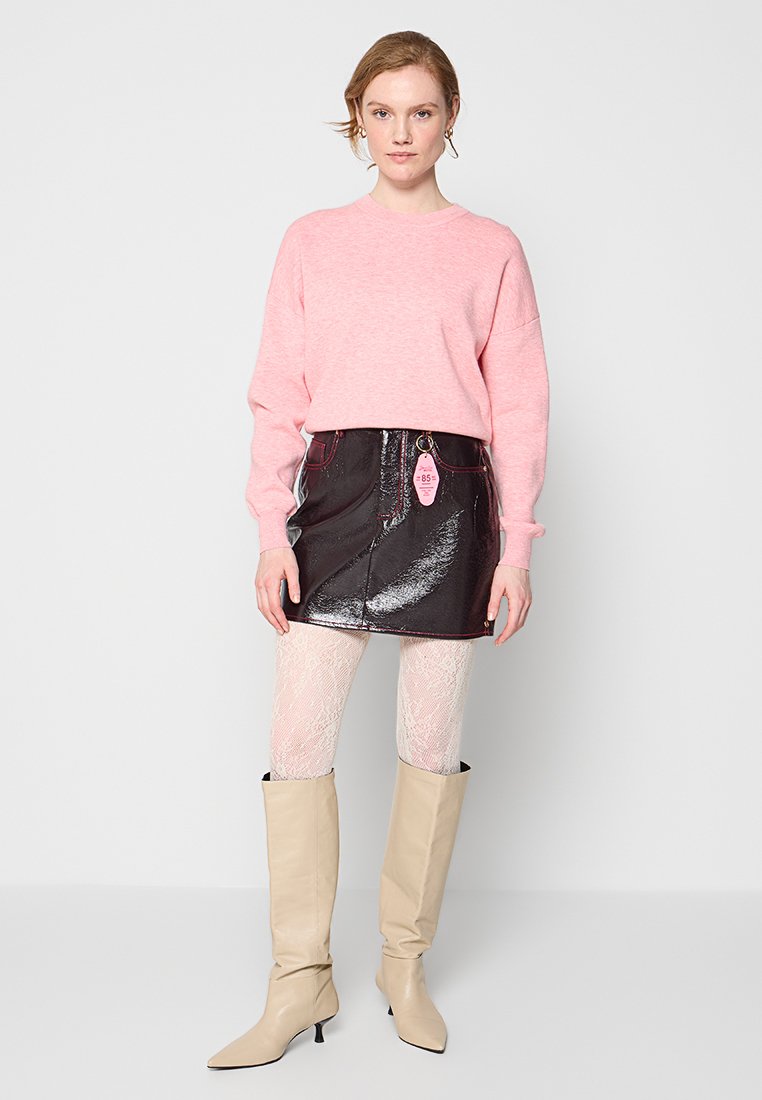 Roze trui, zwarte glanzende minirok met zakken, witte kantencollant, en beige kniehooge laarzen met een spitse neus.