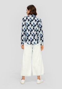 Langarmhemd mit geometrischem Muster in Marineblau, Hellblau und Creme, kombiniert mit weißen Jeans in weitem Schnitt und weißen Sneakern.