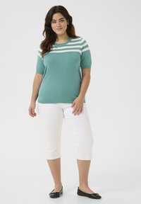 Tricou tricotat de culoare turcoaz cu accente albe pe umeri, asortat cu pantaloni scurți albi și balerini negri. Textură netedă, guler rotund.