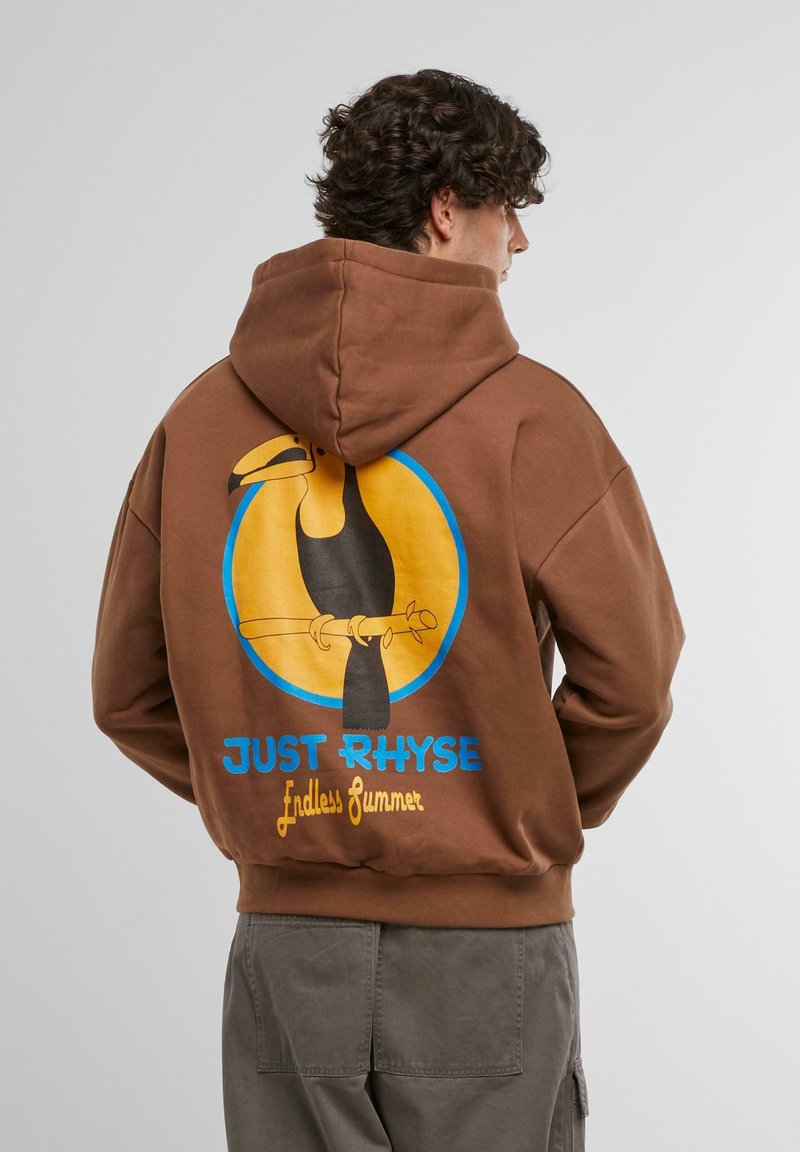 Bruine hoodie met een kleurrafische afbeelding van een toekan tegen een gele cirkel, met de tekst "JUST RHYSE" en "Endless Summer" in blauw en geel.