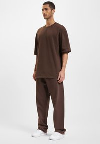 T-shirt oversize marron et pantalon ample assorti, en tissu lisse. Associés à des baskets blanches pour un look complet.