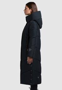 Lange zwarte pufferjas met een hoge kraag, ritszakken en drukknoopsluitingen. Het ontwerp omvat gestikte delen voor isolatie.