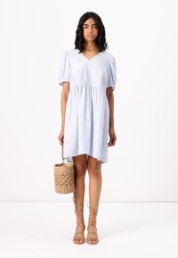 Ανοιχτό μπλε βαμβακερό φόρεμα με κοντά φουσκωτά μανίκια και V-λαιμόκοψη, με φαγωμένα μανίκια και μικρά λουλουδάτα σχέδια. Υφασμάτινη τσάντα καλάθι ως αξεσουάρ.