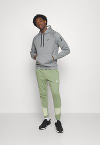 Grå hættetrøje med snore, sort logo på brystet. Lysegrønne joggers, hvide detaljer, sorte sneakers. Enkel atletisk tøjdesign.