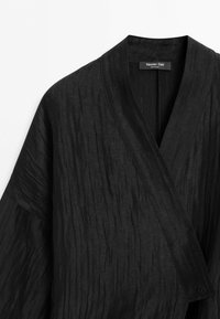 Zwart getextureerde overslagtop met een brede V-hals en een enkele knoopsluiting aan de onderkant rechts, met label Massimo Dutti.