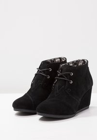 Stivaletti neri in suede con tacco a zeppa, caratterizzati da un design con lacci, fodera in tessuto a motivo e punta arrotondata liscia.