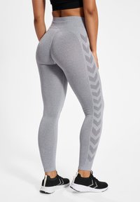 Szare legginsy z wysokim stanem, teksturowany materiał i wzór w jodełkę po zewnętrznych stronach, w połączeniu z czarnymi butami sportowymi.