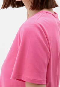 Fuchsia pink t-shirt med rund halsringning och korta ärmar. Tillverkad av ett mjukt tyg, med sydda fållar. Sidoprofilvy.