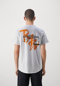 Camiseta de algodón blanca con texto y gráficos en un vibrante color naranja en la parte posterior. Manga corta, cuello redondo clásico, ajuste casual.