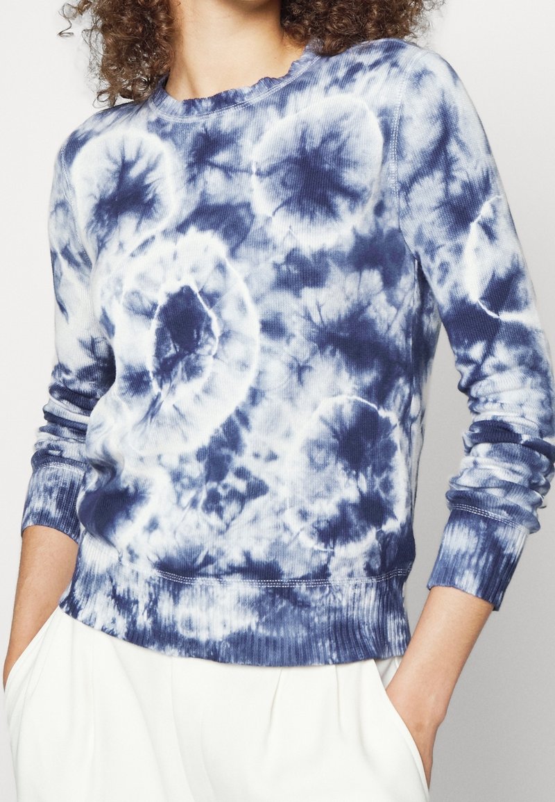 Blå och vit tie-dye tröja med långärmar, med ribbad struktur, rund halsringning och vågig kant vid krage och ärmslut.