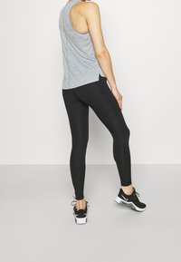 Grå tanktop kombineret med sorte leggings og sorte træningssko. Tanktoppen har en rundet ryg og sideslids for nem bevægelse.