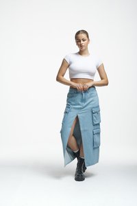 Jeans maxi krilo z nahrbtnimi žepi, svetlo modre barve, z visokim razporkom in gladko teksturo. Ujemajo se z črnimi čipkastimi škornji in belim kratkim topom.