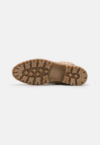 Semelle en caoutchouc brun avec un motif de grip texturé, dotée de crampons multidirectionnels pour une traction et une durabilité. Conception plate et large.