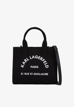 Bolso de tela negra con dos asas superiores y una correa de hombro desmontable. Presenta texto blanco: "KARL LAGERFELD PARIS 21 RUE ST-GUILLAUME."