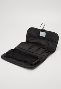 Organizer cosmetico in tessuto nero, con gancio per appenderlo, tasca con zip e scomparto in rete per riporre gli oggetti. Design compatto, texture liscia.