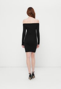 Svart off-the-shoulder kjole med lange ermer, tettsittende design, glatt tekstur og midi-lengde, kombinert med svarte høye hæler.