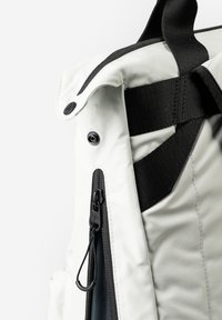Zaino bianco con finitura testurizzata, dotato di una cerniera nera, tracolla e dettagli a pulsante a scatto. Cuciture dettagliate e design elegante.