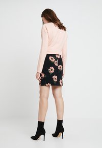 Rosa tröja och svart blommig kjol med rosa blommor. Modellen bär svarta klackade ankelskor. Tight passform. Mjuk textur.