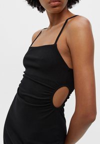 Schwarzes geripptes Kleid mit dünnen Trägern, seitlichen Ausschnitten und gerafften Details an der Taille. Figurbetonte Silhouette mit glatter Textur.