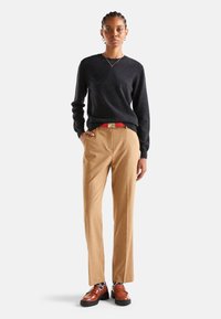 Czarny dziany sweter, beżowe eleganckie spodnie, czerwony pasek, brązowe skórzane buty z karbowaną podeszwą i wzorzyste skarpetki. Prosty, elegancki design.