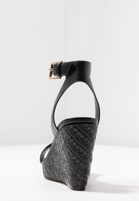 Černé wedges sandály s texturovanou tkanou patou. Mají kožený náramek na kotníku se zlatou sponou, otevřený design a hladkou podrážku.